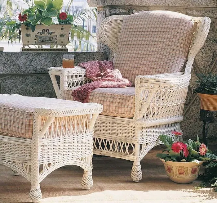 Sillón y reposapiés de mimbre blanco con cojines de cuadros en una terraza con plantas