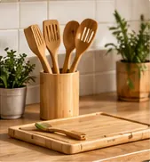 Utensilios de cocina de bambú en un bote junto a una tabla de cortar