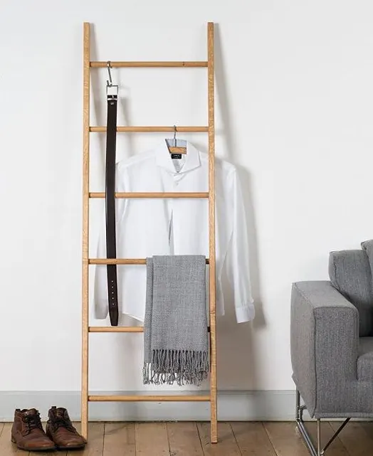 Escalera decorativa de bambú apoyada en la pared con una camisa, un cinturón y una manta colgados