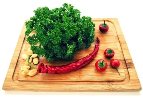 Tabla de cortar de bambú con perejil, guindillas, tomates cherry y ajos